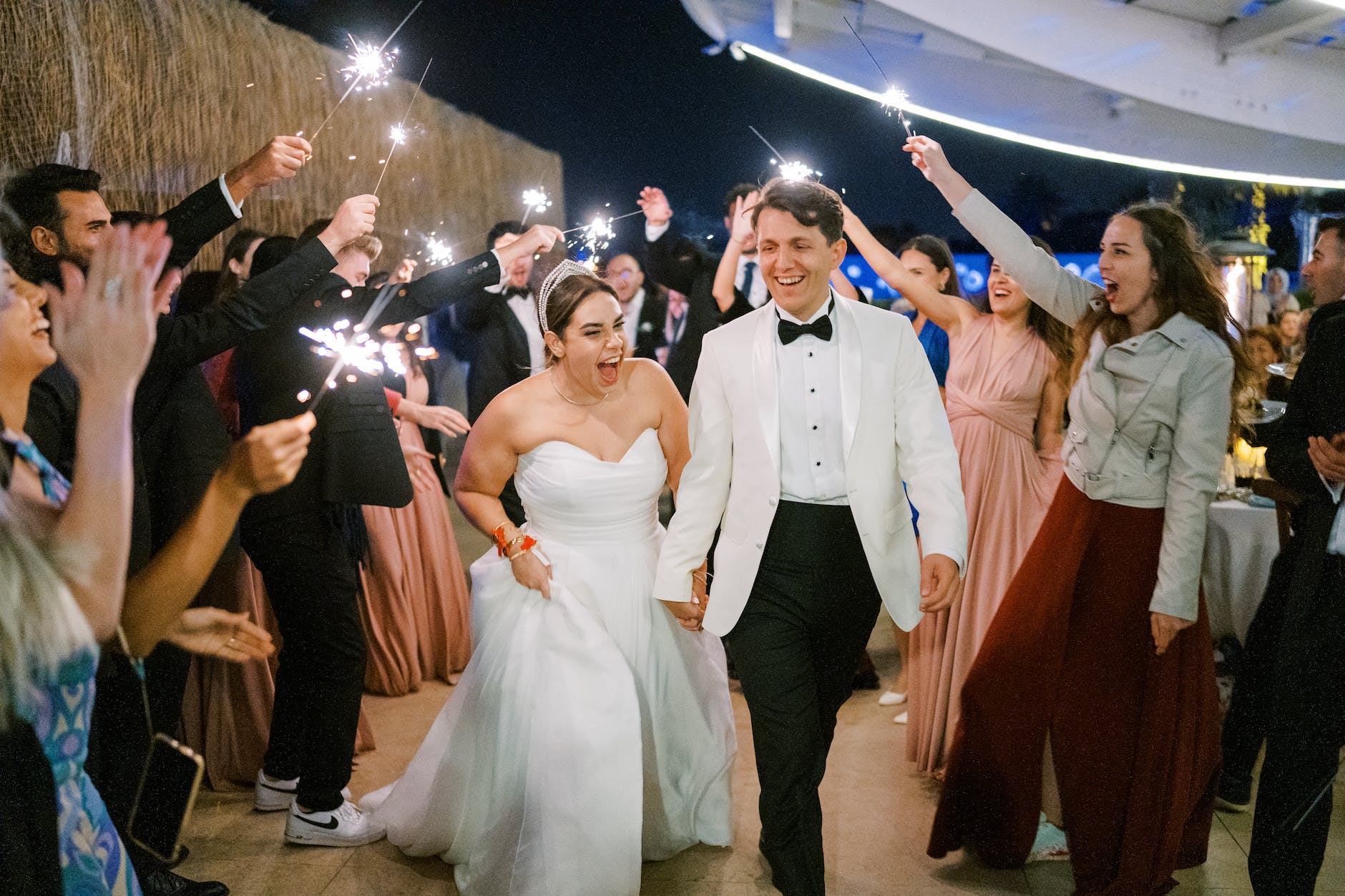 newlyweds walking under people holding sparklers in raised arms