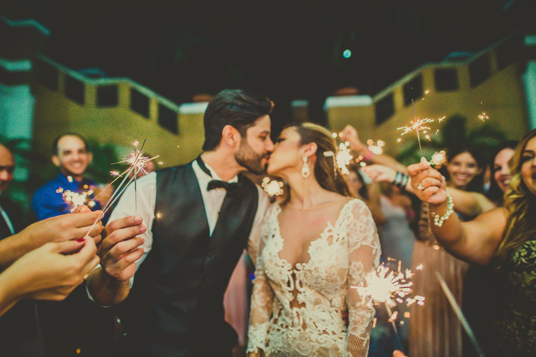 photo of couple kissing near people holding sparklers